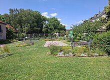 Für Anwohner*innen nutzbare Grünfläche inmitten von Wohnbebauung mit Blumenstreifen und Bouleplatz