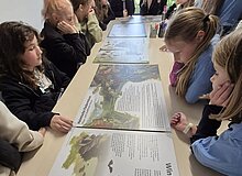 Vesperto Fledermausschutz_Duisburg_Tom Perkowski_2025 Kindergruppe sitzt um mehrere Fledermaus-Bildtafelm die auf einen Tosch liegen