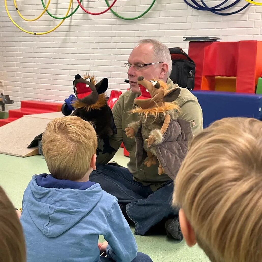 Vesperto Fledermausschutz_Duisburg_Tom Perkowski_2025 Mann sitzt mit zwei Fledermaus-Handpuppen vor Kindern einer KiTa Gruppe