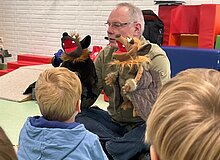 Vesperto Fledermausschutz_Duisburg_Tom Perkowski_2025 Mann sitzt mit zwei Fledermaus-Handpuppen vor Kindern einer KiTa Gruppe