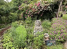 Wildrosenhecke, davor Steinturm und Staudenbeet