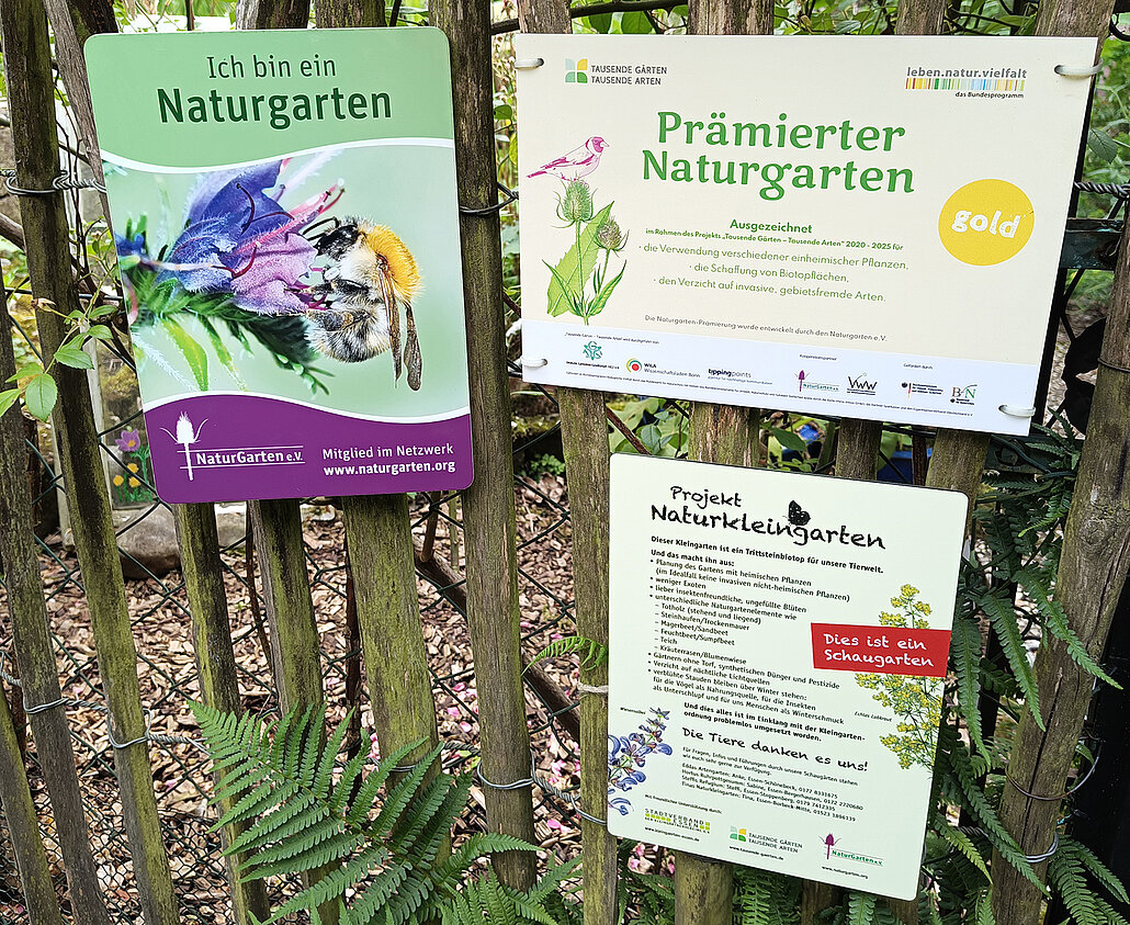 Schilder am Gartenzaun: Mitglied im Naturgartenverein, Gold-Prämierung des Gartens, Projekt Naturkleingarten
