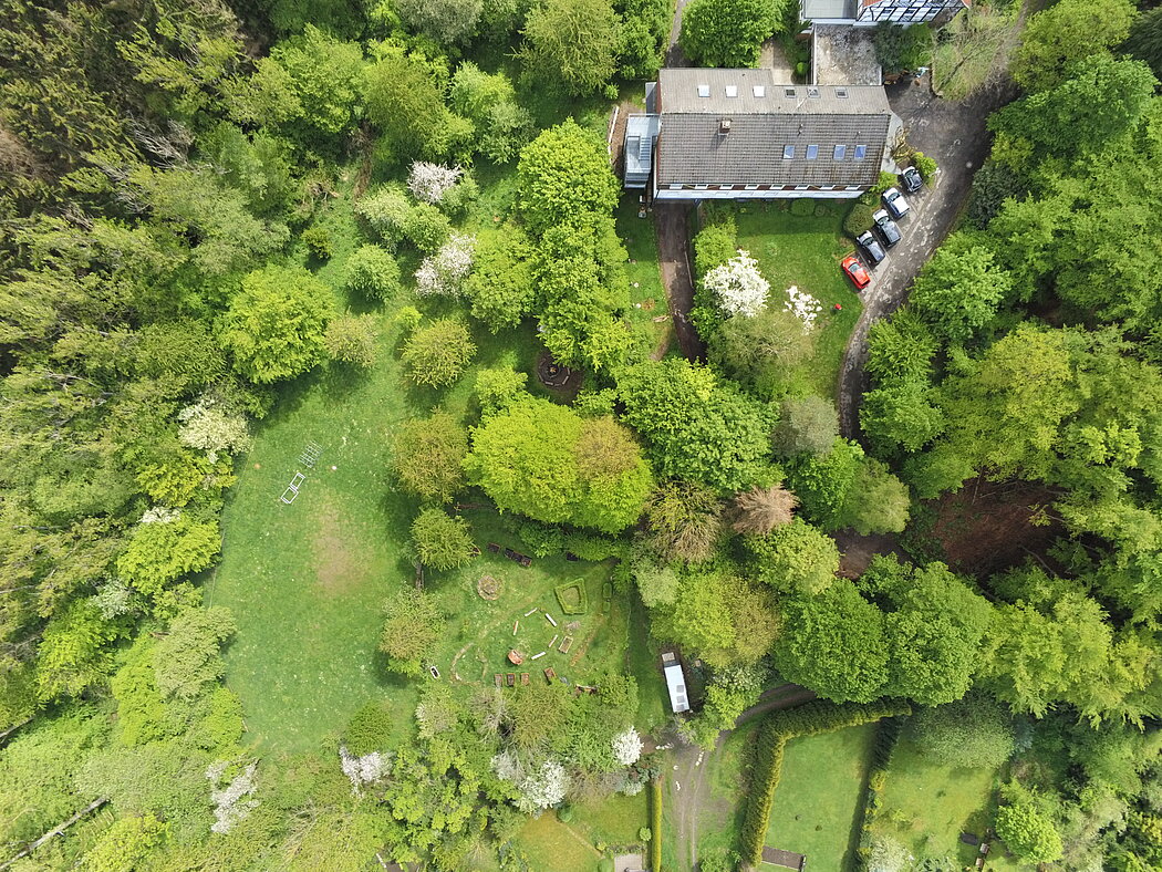 Marienhofgarten_Hagen_SilkeKrüger_2025 Blick aus dem Himmel auf grüne Rasen und Baumfläche. Dachfläche des Hauses ist etwas zu sehen