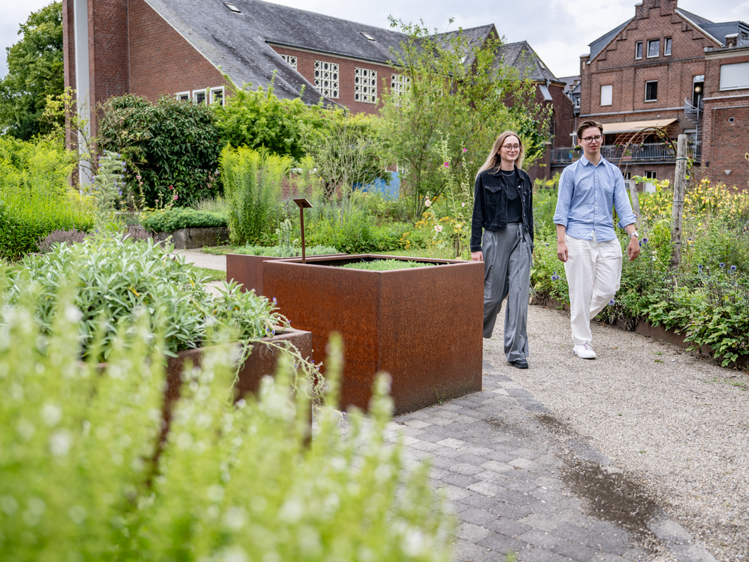 Zwei junge Menschen laufen durch den Garten von St. Bernardin in Sonsbeck, altes Klostergebäude im Hintergrund