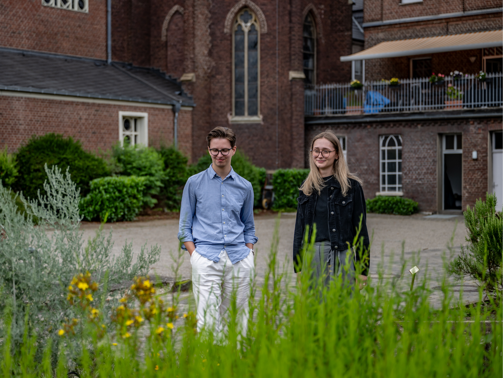 Zwei junge Menschen laufen durch den Garten von St. Bernardin in Sonsbeck, altes Klostergebäude im Hintergrund