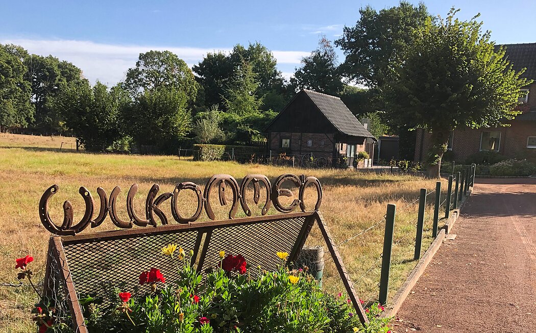 Landleben op de Kuhle, Dorsten, L.Demmer, 2025 Willkommensschild aus Hufeisen mit Blick auf das Fachwerkhäuschen.