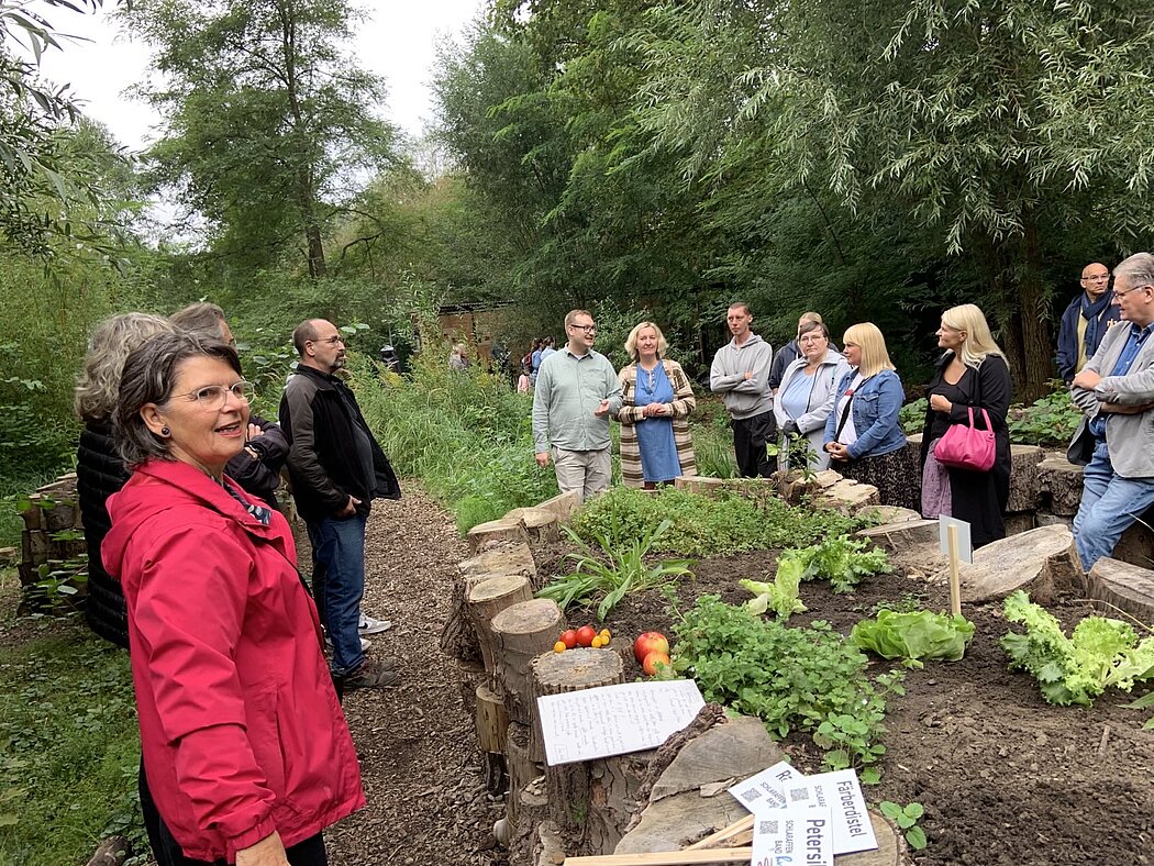 Viele Menschen stehen um Hochbeete aus Baumscheiben herum.