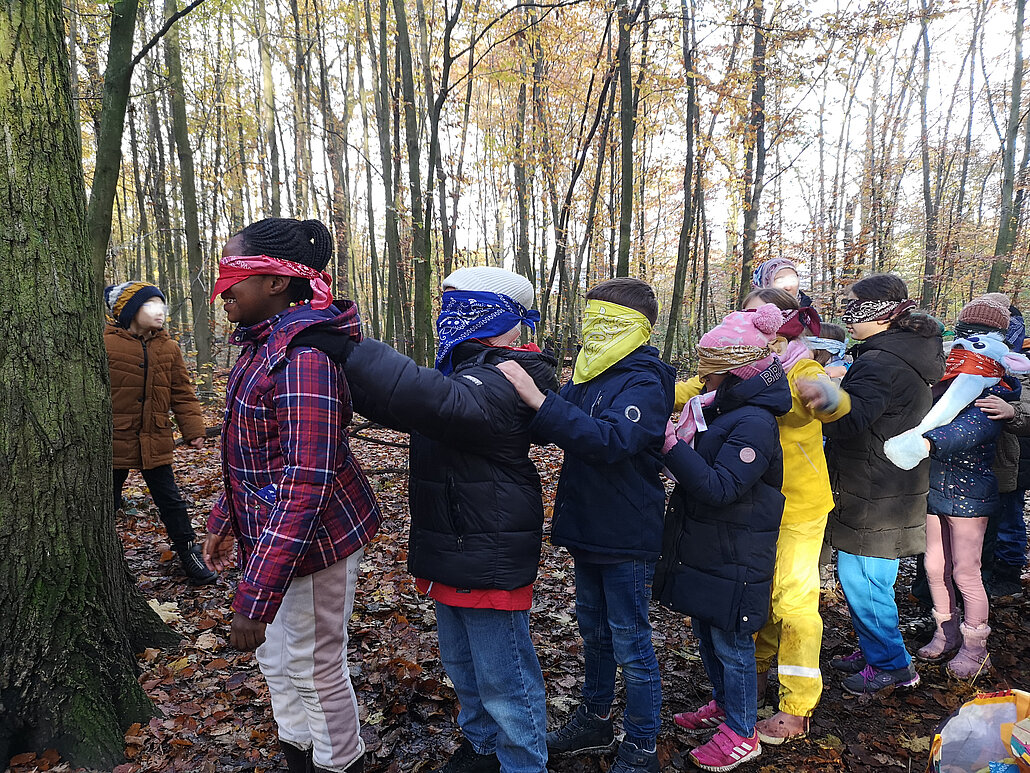 Grünes Klassenzimmer Duisburg Grundschulklinder stehen mit verbundenen Augen hintereinander vor einem Baum
