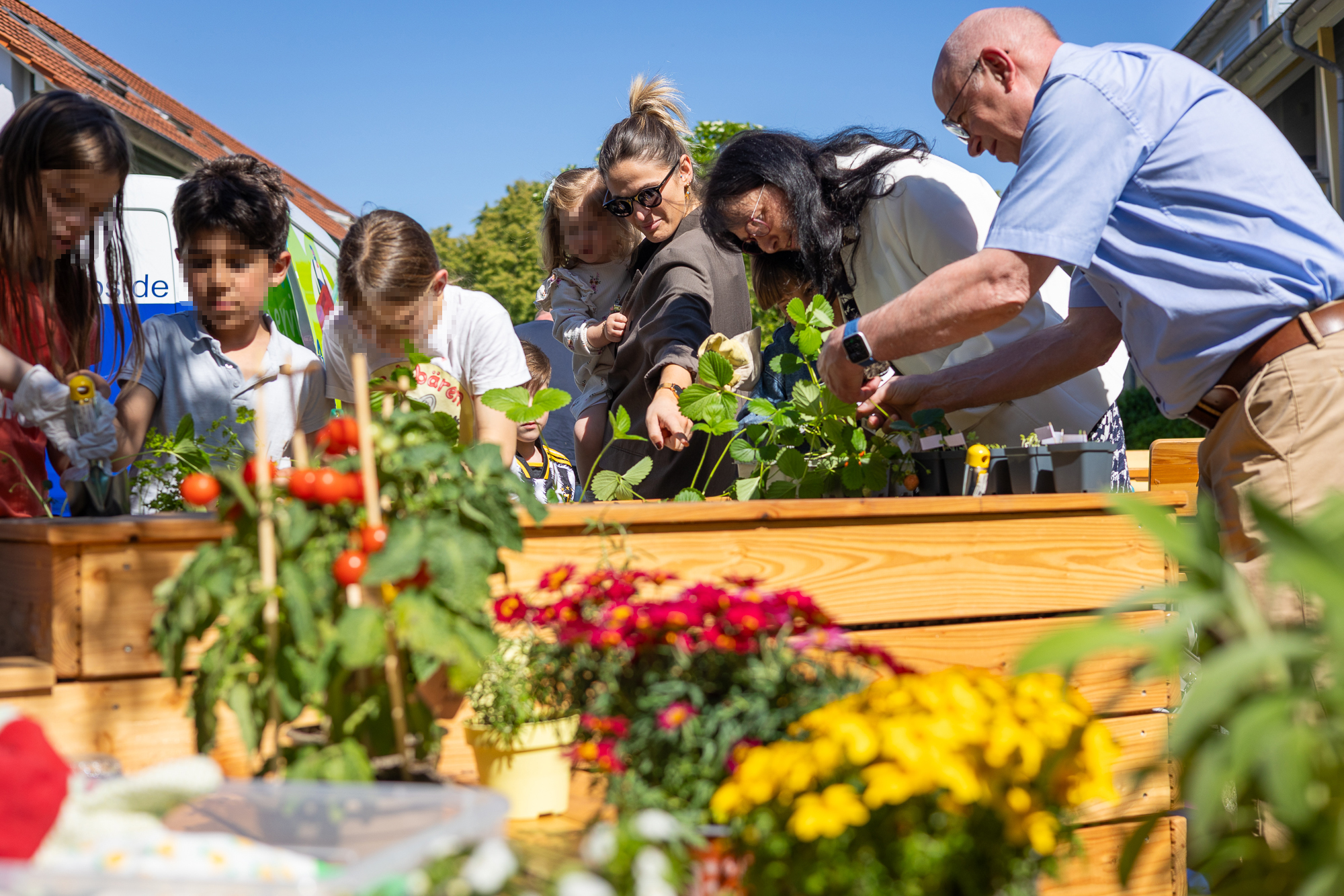 Im Vordergrund bunte Blumen, im Hintergrund mehrere Menschen, die über ein Hochbeet gebeugt sind
