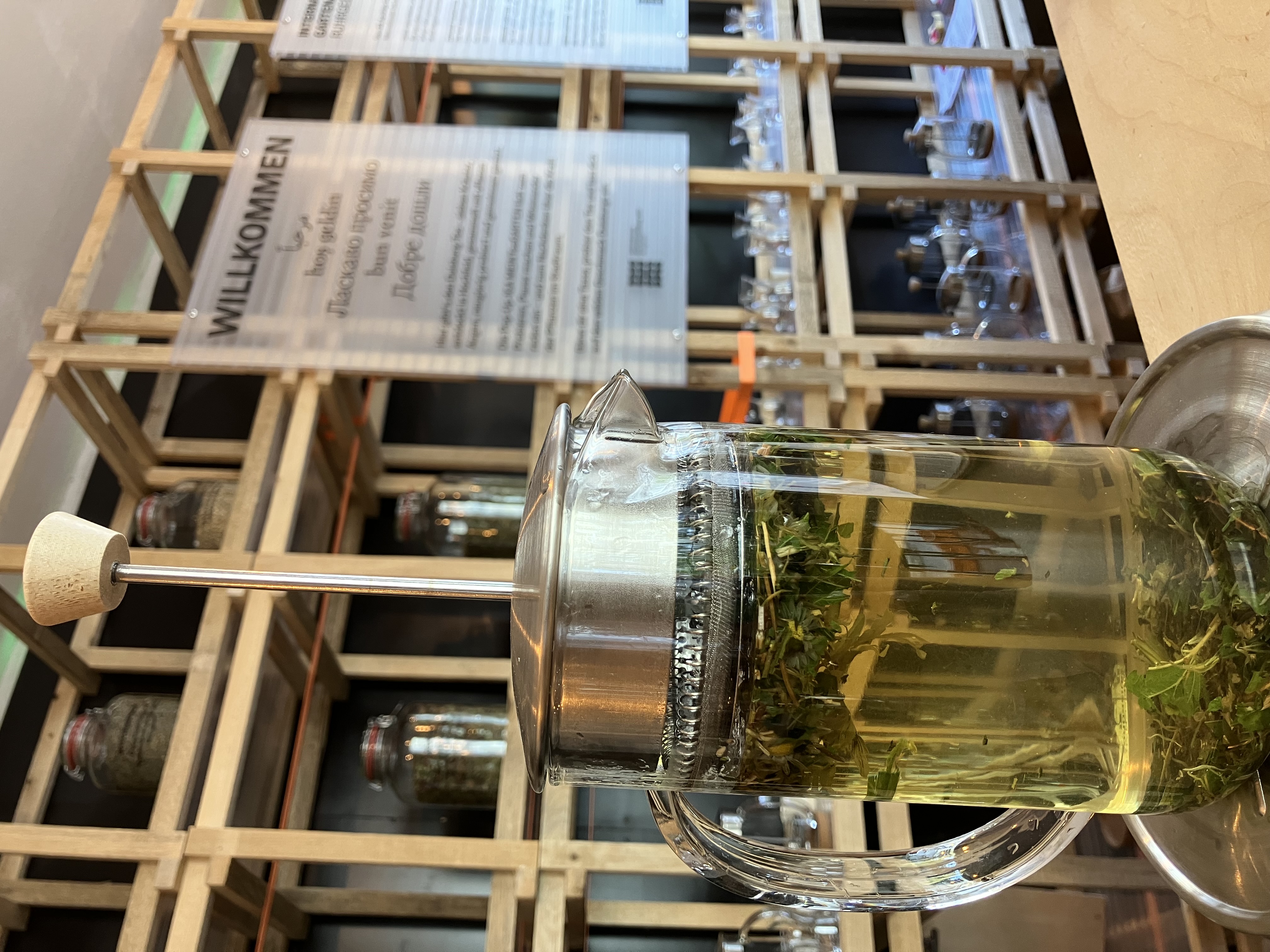 Innenansicht der Pop-Up-IGA Duisburg. Eine Teekanne mit Tee steht auf dem Tresen, im Hintergrund sind Tafeln zu sehen mit der Aufschrift "Willkommen".