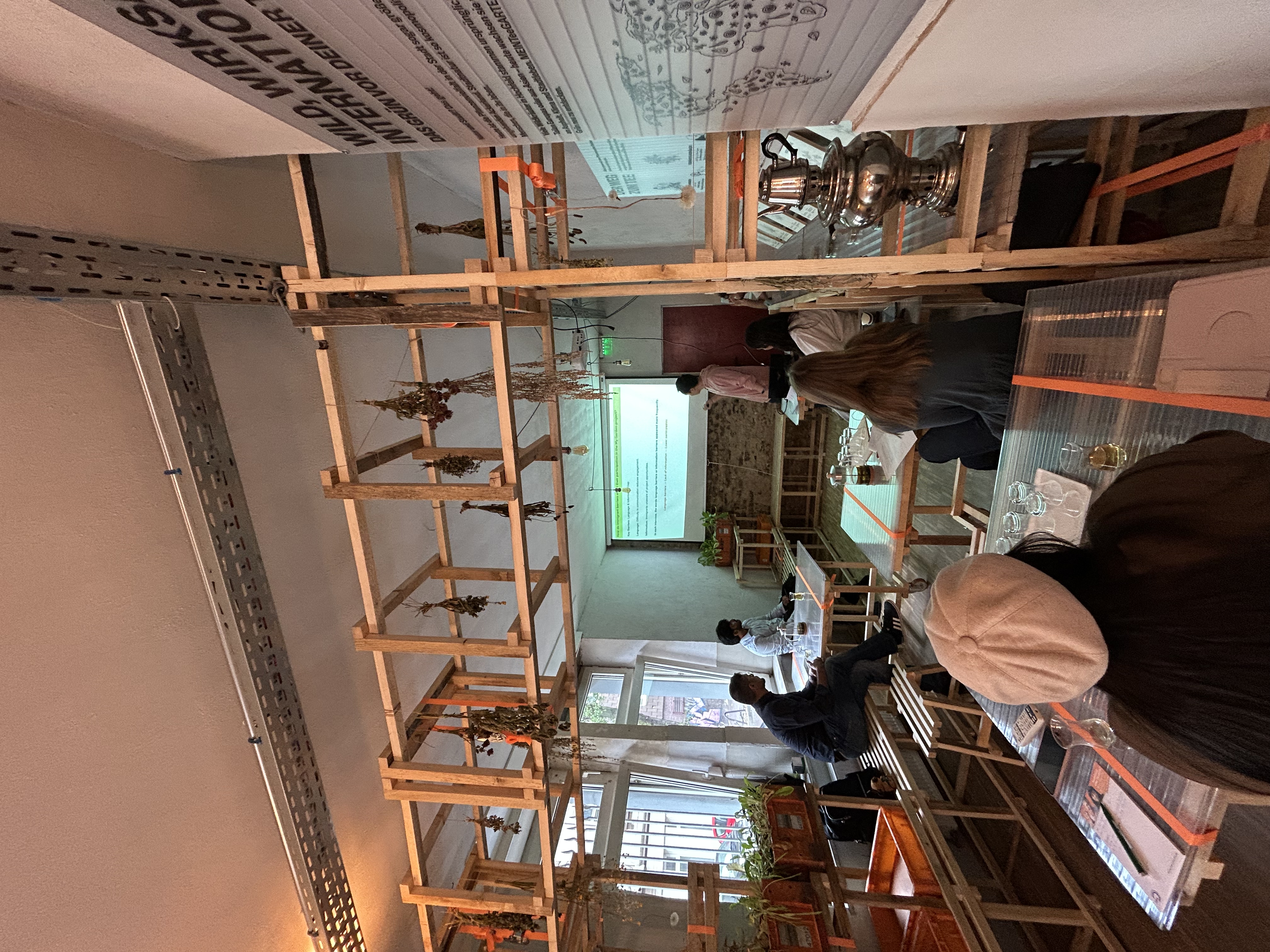 Innenraum der Pop-Up-IGA Duisburg während eines Seminars der TU Dortmund. Mehrere Studierende sitzen an Tischen und schauen auf eine Leinwand, auf die etwas mit einem Beamer projiziert wird. 