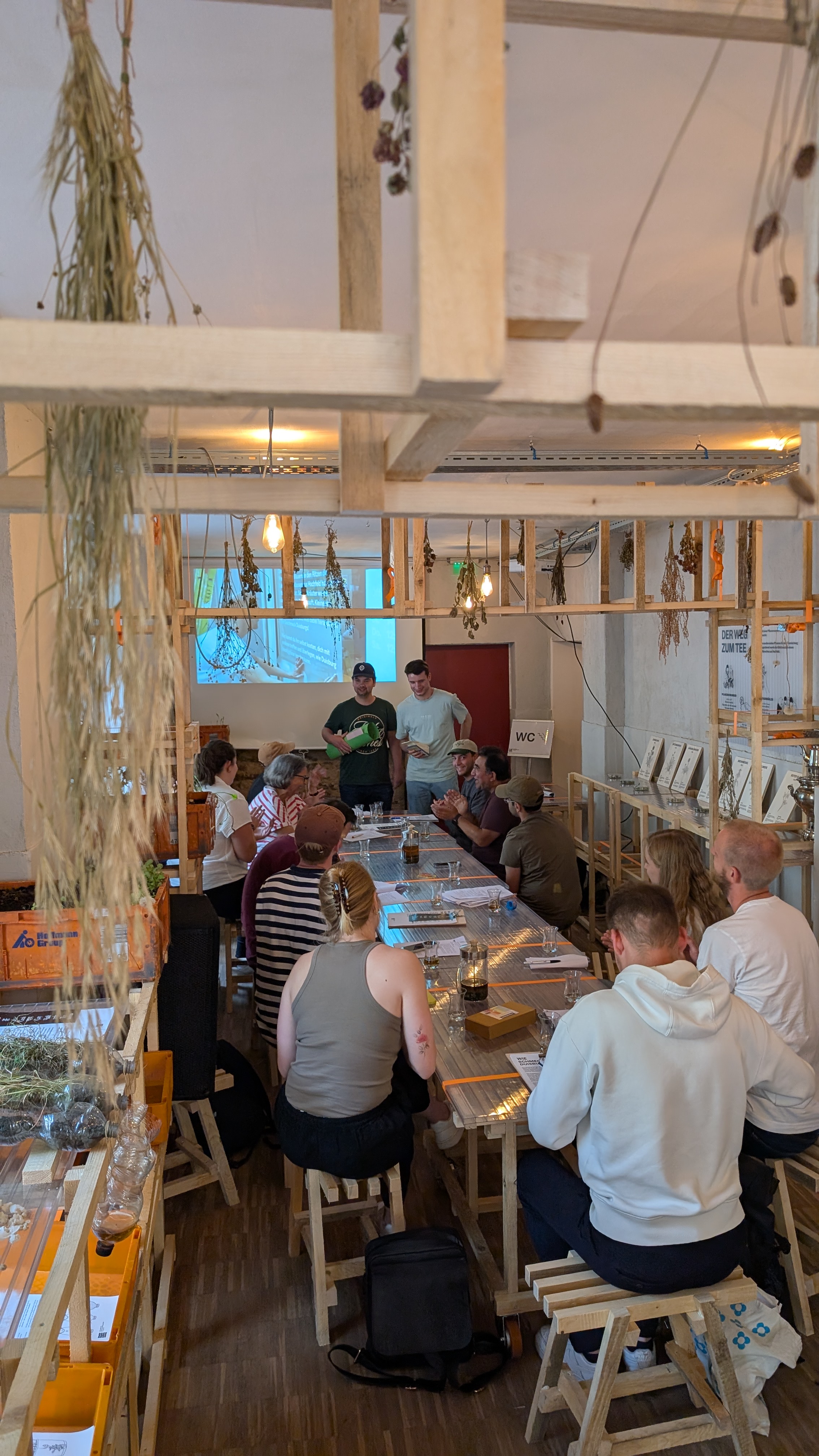 Innenansicht der Pop-Up-IGA Duisburg während eines Seminar der Ruhr-Universität-Bochum. Rückansicht von mehreren Studierenden, die an Tischen sitzen und auf eine Leinwand sehen, auf die etwas von einem Beamer projiziert wird.